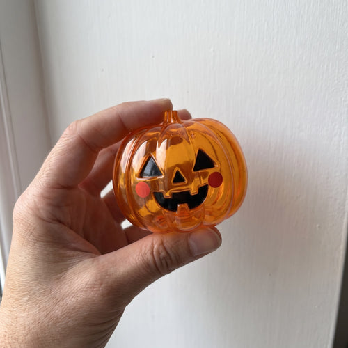 GRIN, the translucent orange jack-o-lantern squishy, held in an adult hand